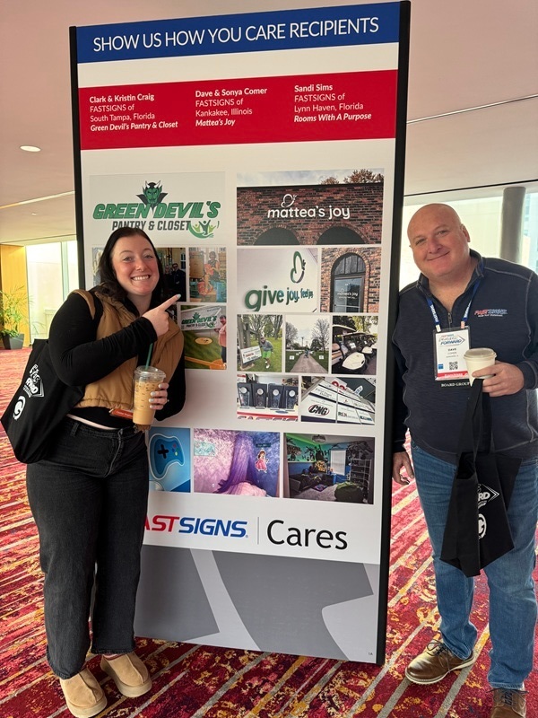 An image of the owners next to a FASTSIGNS Show Us How You Care Recipients banner.